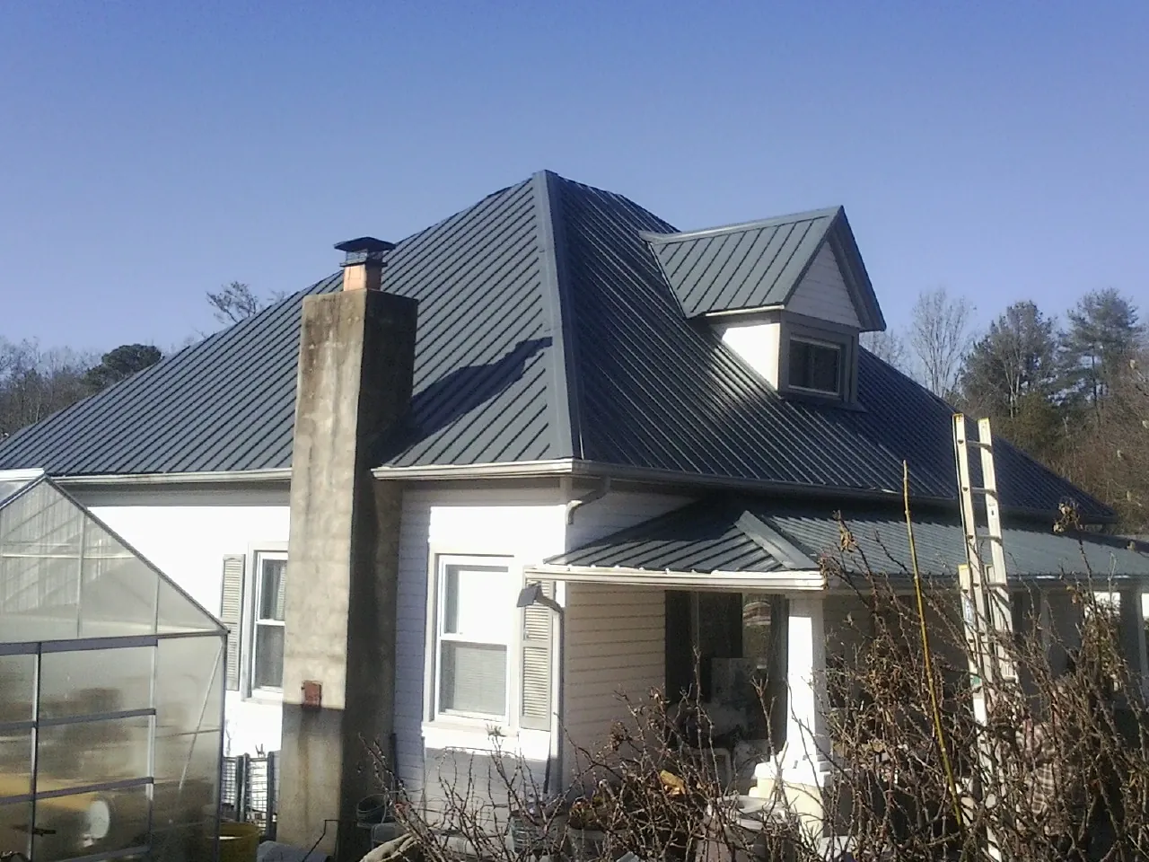 Dark blue standing seam metal roof on a white farmhouse with dormer — Slate & Tile Roof Repair by Roofing Brothers in Garvin