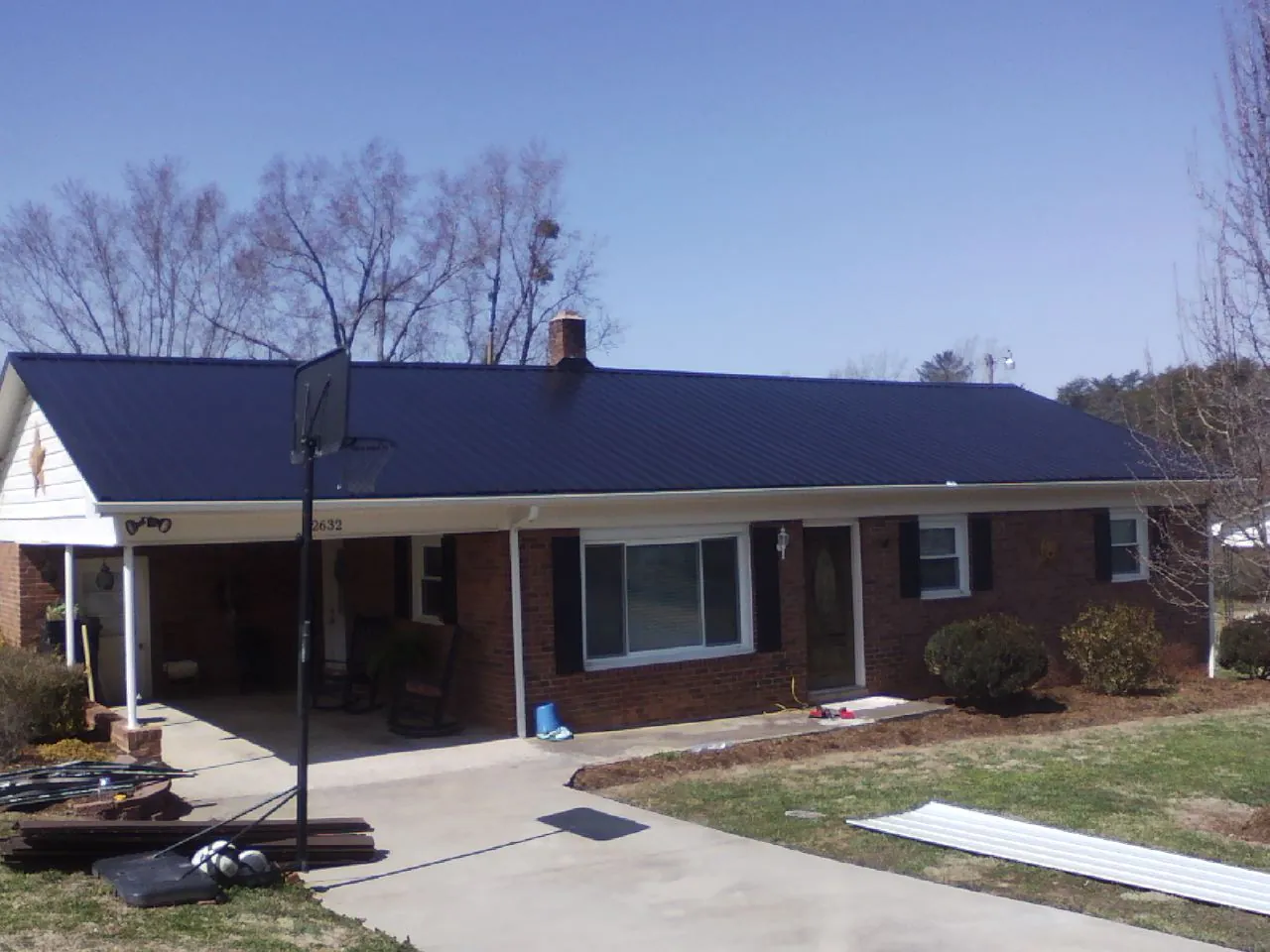 Finished dark blue metal roof on a brick ranch with a carport in Garvin